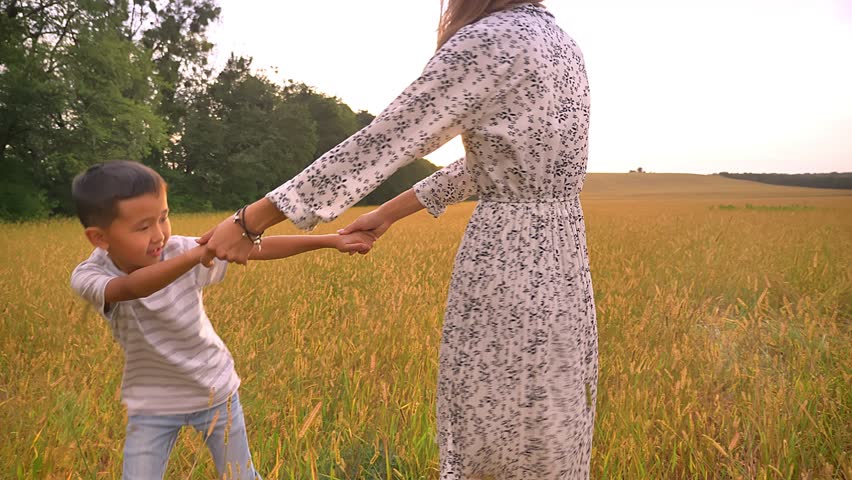 Lovely asian mother spinning with her little fellow on wheat field