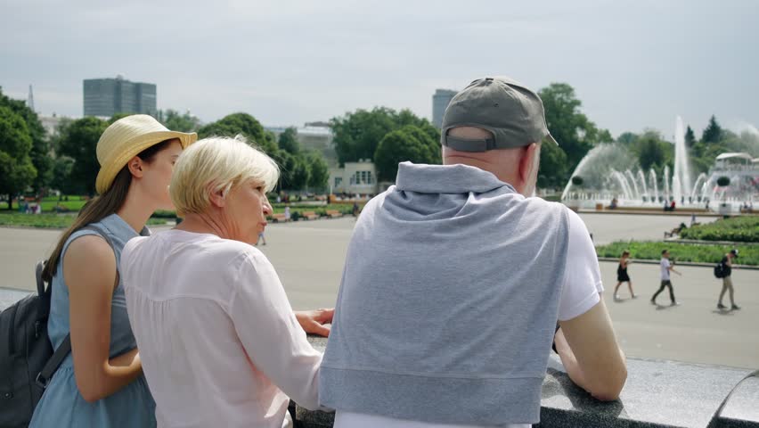 Back view of happy family enjoying summer vacation together in Moscow, Russia. Seniors with young teenage daughter having great time standing in Gorky Park laughing and chatting sightseeing