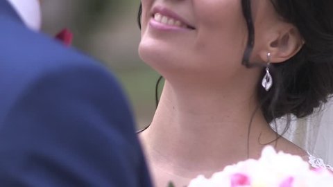 Happy dark-haired bride and tall groom dark-blue suit, Wedding boutonniere of freesias  and bow tie on looking into each other's eyes smiling, hugging, close-up