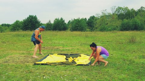 A man and a woman stick the pegs of the tent into the ground.