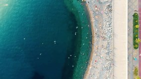 Picturesque timelapse of pebble beach life in Sochi view from above. Beautiful green and blue sea waves roll ashore, people swim in the water and sunbathe on the shore crammed with colorful umbrellas.