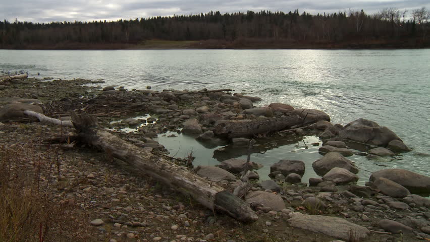Driftwood and large stones on the shore of the North Saskatchewan River in Edmonton, Canada, on a grey fall afternoon.
