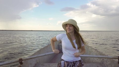Beautiful young woman rower in straw hat sailing slowly on paddle boat in calm river seascape skyline
