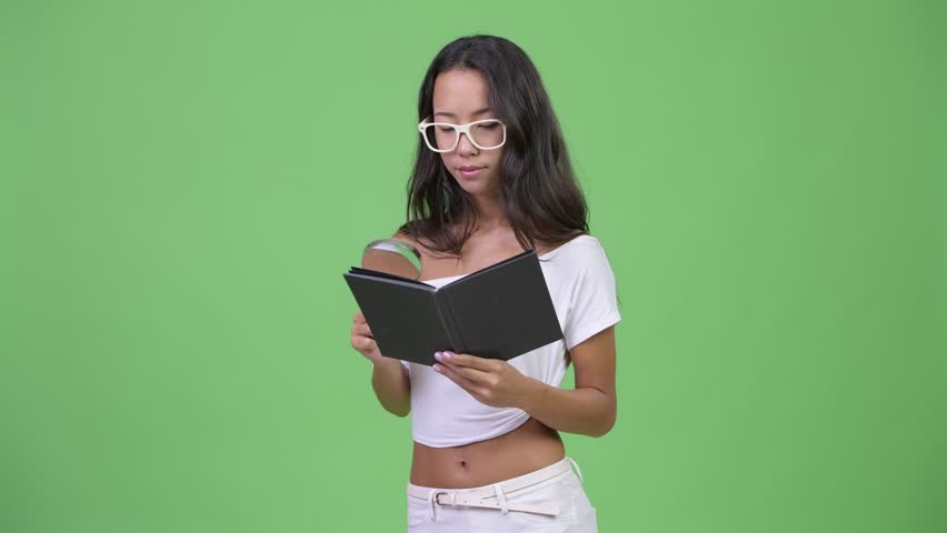 Young beautiful multi-ethnic woman reading book with magnifying glass and eyeglasses