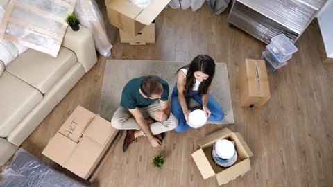 Top view young woman unpacking from cardboard boxes next to her husband in their new house