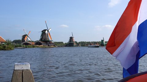 Traditional Holland Windmills and Floating Flag in Zaanse Schans, Netherlands. Touristic Village near the Amsterdam with the windmills and historical Dutch Houses