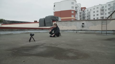 Handsome reporter sitting in pose of lotus shooting a video by himself on the street roof. 4K