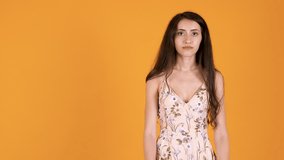 Woman in summer dress saying NO with gestures while looking at the camera. Unsatisfied girl isolated on orange yellow background in studio