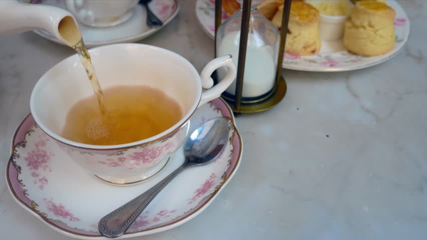 Pouring english tea into the beautiful english tea cup with background of sweet dessert (scone)