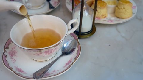 Pouring english tea into the beautiful english tea cup with background of sweet dessert (scone)