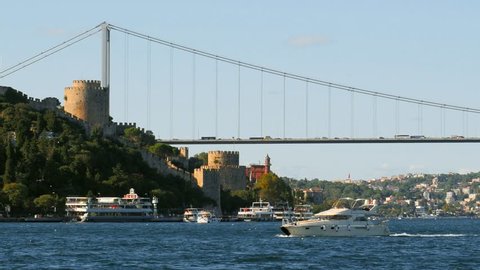 Istanbul Perili Kosk and Rumeli Hisari Fortress Bosphorus Straits. Yusuf Ziya Pasha Kiosk, Istanbul, Turkey. Luxury white yacht sails past the historical castle. 4K Cinematic, Zoom out telephoto shot
