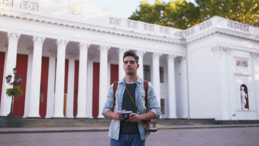 Young attractive handsome man tourist with backpack taking photos on vintage camera in old city center