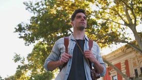Portrait of young attractive handsome man tourist with backpack in city center, slow motion, low angle view