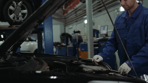 Mechanic checking oil level in a car workshop man portrait engine car repair service