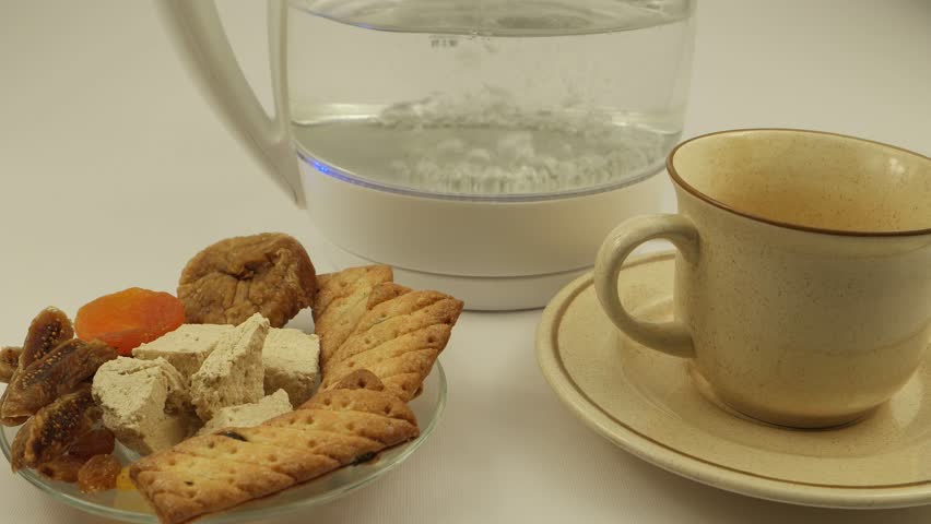 Cream cup and saucer with cookies and oriental sweetness on the background of a boiling glass electric kettle