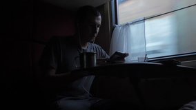 man silhouette is sitting on the train carriage holding a smartphone Railway and drinking coffee and tea. slow motion video. man writes messages in the smartphone in the train social media. man with