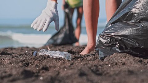 Group of volunteers cleaning up beach. The volunteer raises and throws a plastic bottle into the bag. Volunteering and recycling concept. Environmental awareness concept copy space