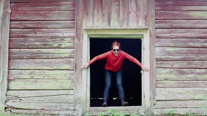 Women with a smile and sunglasses jumping out from the entrance of the old farmhouse.  
