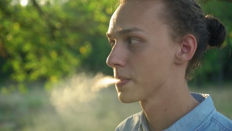 young cute man with tied hair smoking cigarette outdoors, sunset, 4k 4