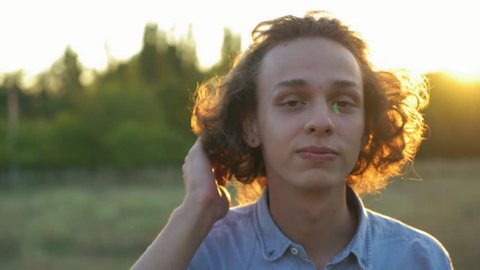 extraordinary curly man touches his long hair outdoors, sunset, 4k 3