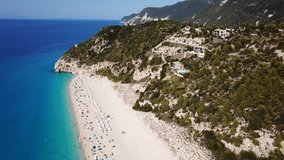 Aerial drone bird's eye view video of popular beach of Milos with turquoise clear waters and sun beds, island of Lefkada, Ionian, Greece