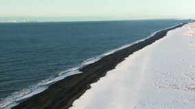 Aerial view crashing waves breaking on black sand beach in Iceland during winter with snow