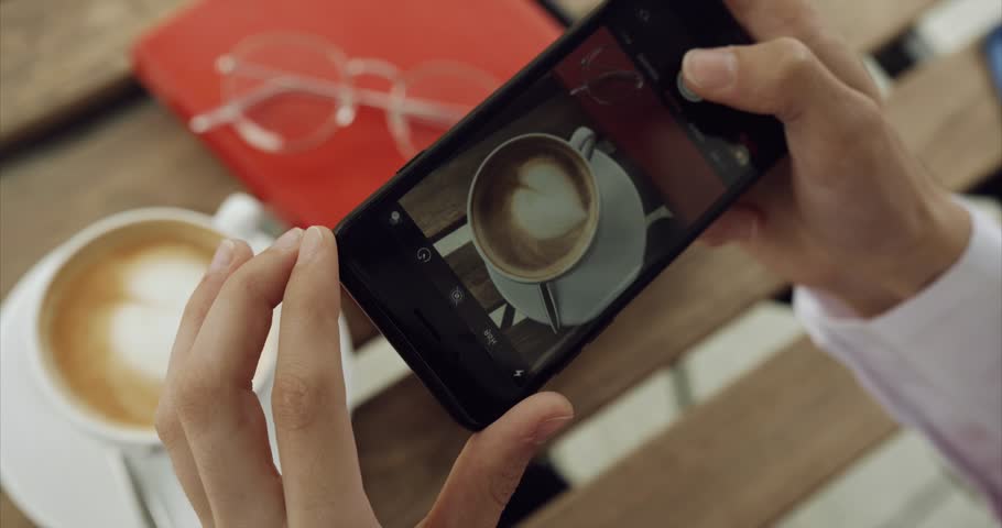 Girl takes a photo of coffee, notebook and glasses for social media on her phone