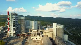 Aerial view of cement factory, large industrial building in the mountains. Concept of cisterns, pipes, metal structures, concrete production. Daytime footage with a beautiful blue sky.