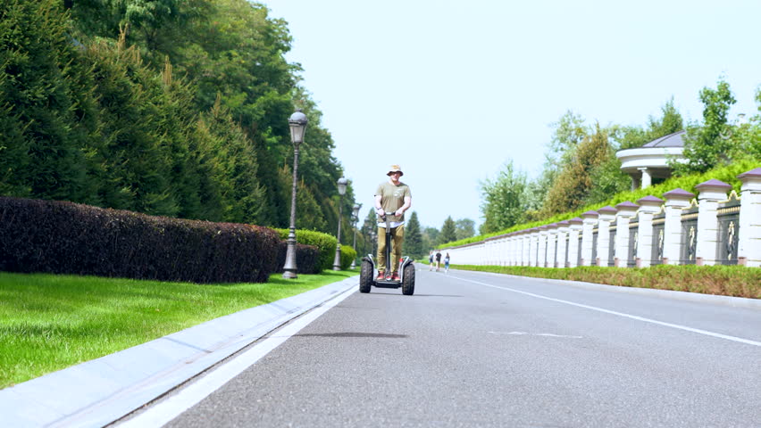 Man riding a Electric Personal Transporter in a low angle view approaching then passing the camera on a quiet road