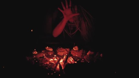 Scary witch does voodoo black magic ritual near the fire at night. Halloween horror 