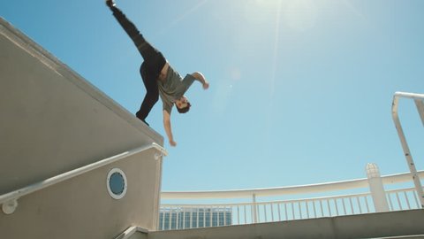 Slow motion parkour athlete in urban city doing extreme front flip off ledge with lens flare