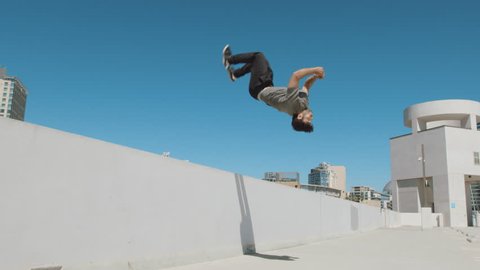 Slow motion parkour athlete doing extreme backflip off wall in urban city outside isolated in sky