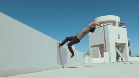 Parkour athlete running up urban wall doing extreme backflip outside isolated in sky