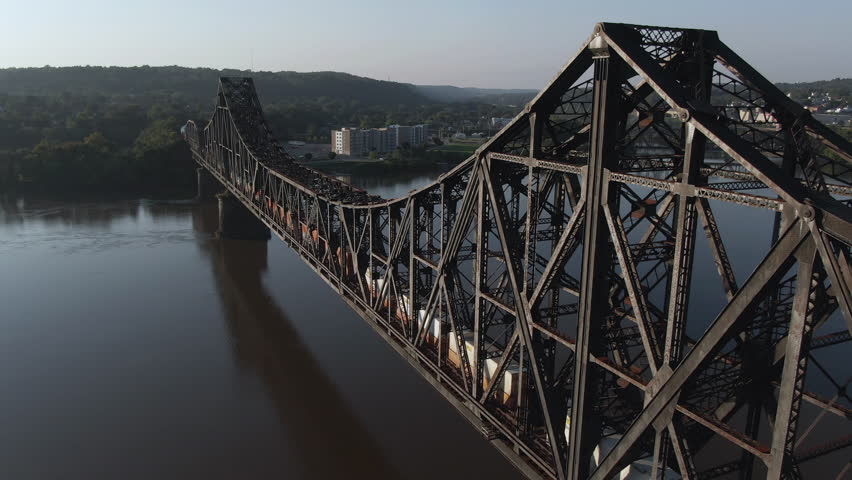 A high angle aerial profile view of a cargo train traveling over a railroad bridge spanning the Ohio River. Pittsburgh suburbs.  	