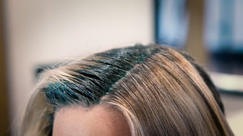 Tight Close Up of a blonde girl getting blue hair dye applied to roots on top of her head for unicorn hair style at a salon.