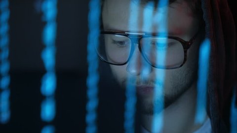 The programmer in glasses works at the computer over the program in a dark room night. Smooth blue illumination. Reflection in glasses. ProRes 422