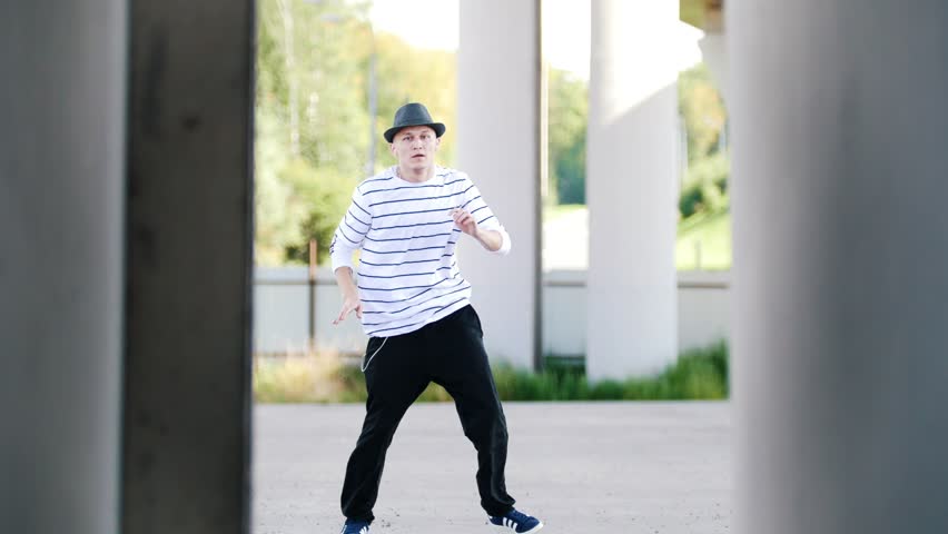 Popper moves to the music with headphones on the street in the middle of two walls on a sunny summer day