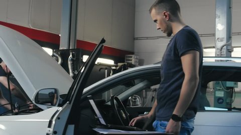 Technician man making computer diagnostics car engine in repair shop. Car mechanic using tools for repair automobile. Auto mechanic working in repair garage. Chip tuning