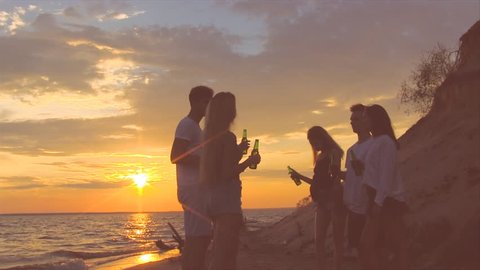 Friends clinking beer bottles on the beach during the sunset.