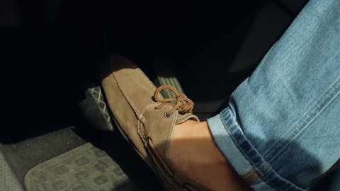 Close-up of male driver foot in shoes pressing brake pedal while driving car on road. Man foot pressing car brake pedal to avoid car accident during a drive.