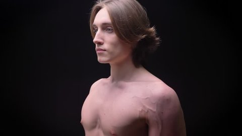 naked young caucasian boy standing in profile and looking at camera focused on black background