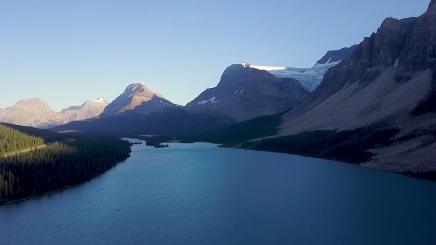 Aerial shot above lake next to road with mountains and forest while sunset in Rocky Mountains in Canada