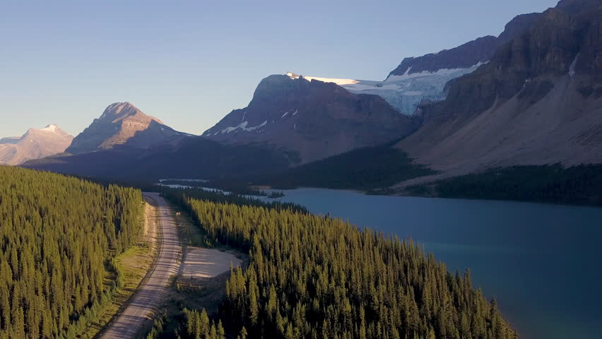 Aerial shot above lake next to road with mountains and forest while sunset in Rocky Mountains in Canada