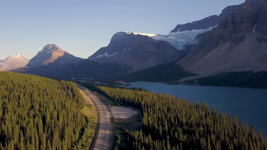 Aerial shot above lake next to road with mountains and forest while sunset in Rocky Mountains in Canada