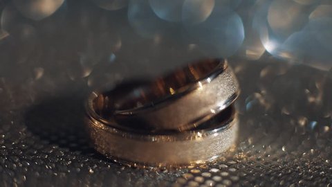 Wedding rings lying on shiny golden shining surface with light, close-up macro footage. Rotate spinning clockwise. Pair of marriage symbols. Love of bride and groom, wife and husband. Matrimony symbol