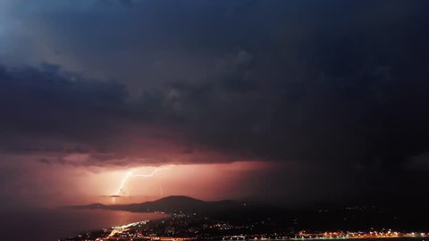 Timelapse of beautiful thunderstorm with picturesque lightning illuminating the sky with pink and orange colors. Many dramatic lightning flashes on the stormy sky over the night coastal city.
