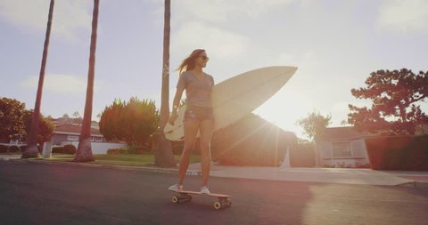 Surfer girl riding skateboard down street at sunset with lens flare