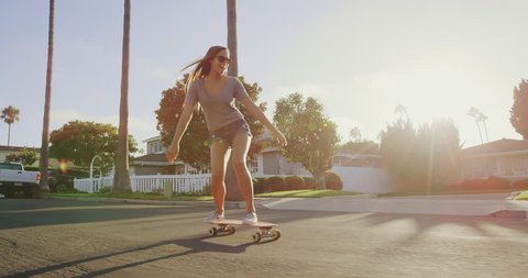 Happy care free girl skateboarding down street at sunset with hands up in air
