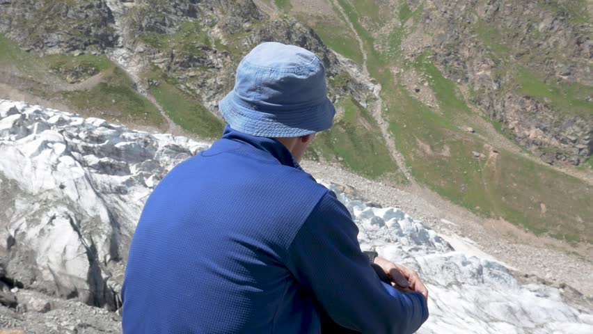 A man sits on a mountain and looks at the glacier from a height