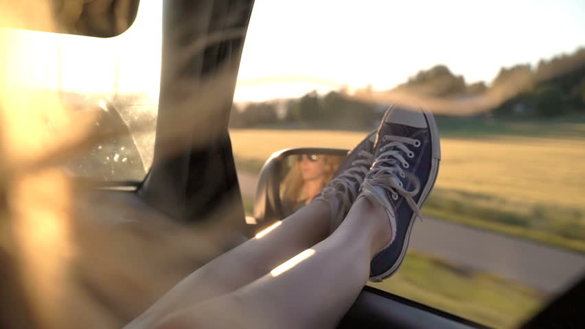 A young redhead woman enjoys traveling in a car by sticking out her legs in an open window. Slow motion. Royalty-Free Stock Footage #1016690836